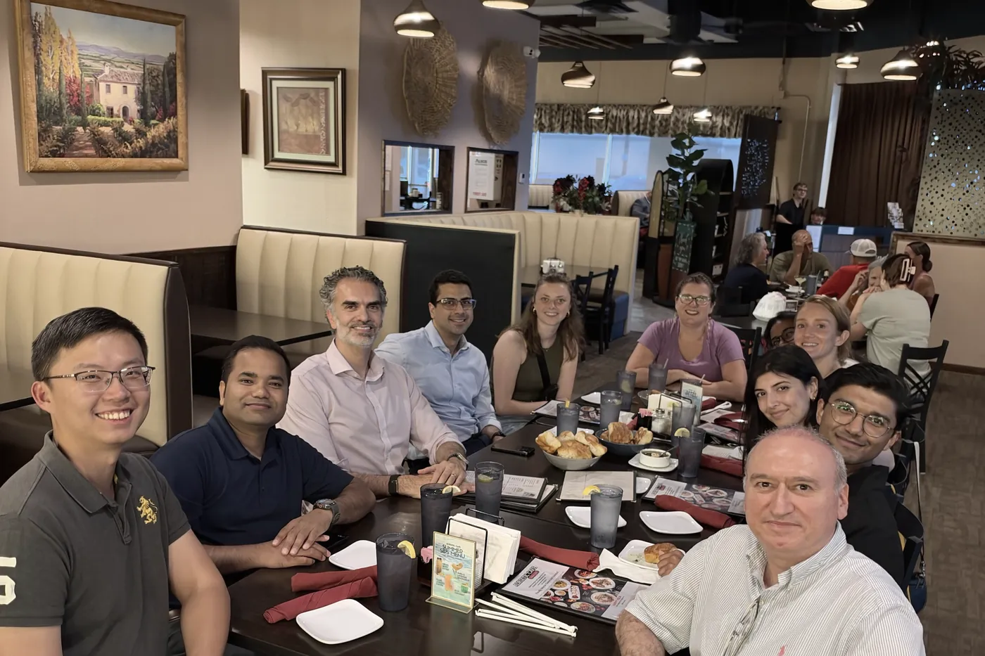 About a dozen lab members seated around a long restaurant table, smiling at the camera